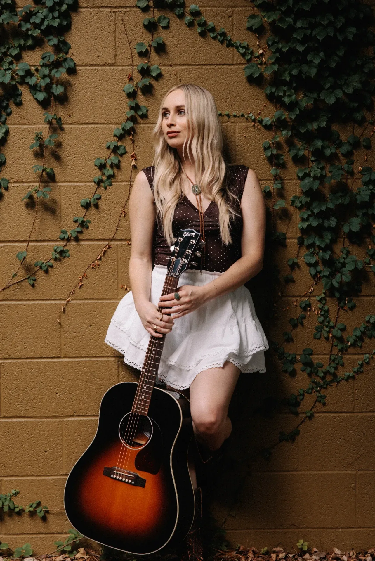 Melanie Dyer with her guitar against an ivy-covered wall